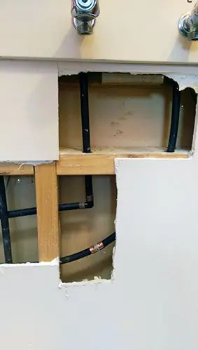 Copper vs plastic piping replacement wellington. Replacement of leaking water piping. Image of wall open showing leaking water piping.